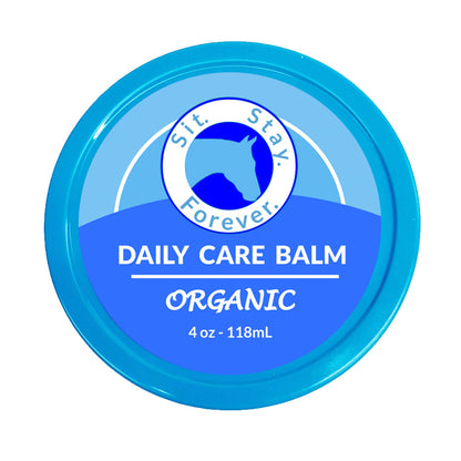 Blue round container labeled Sit. Stay. Forever. DAILY CARE BALM ORGANIC 4 oz - 118 mL. The product is an organic care balm for horses. The label features the logo with a silhouette of a horse.