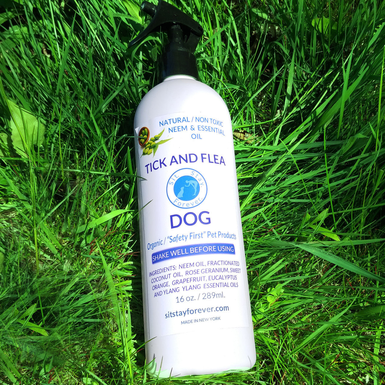 Sit.Stay.Forever. Tick and Flea spray for dogs placed in grass. The bottle is 16 oz (289 ml) and features natural, non-toxic neem and essential oil. The label includes the Sit.Stay.Forever. logo and mentions organic "Safety First" Pet Products. Ingredients listed: neem oil, fractionated coconut oil, rose geranium, sweet orange, grapefruit, eucalyptus, and ylang-ylang essential oils.