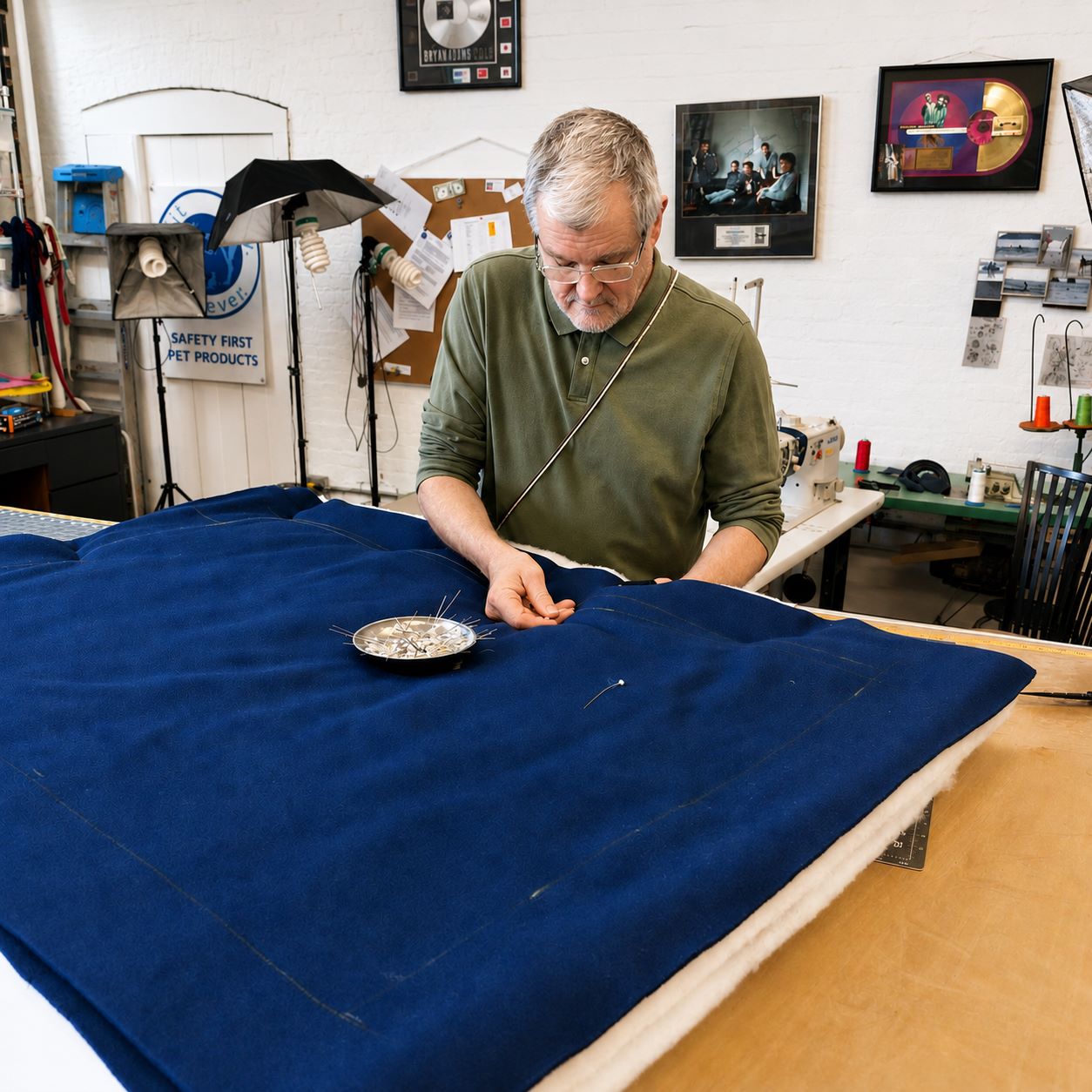 Man working on a  navy blue Sit Stay Forever square fleece dog bed in the company shop in the Dana Warp Mill wih sewing machines in the background