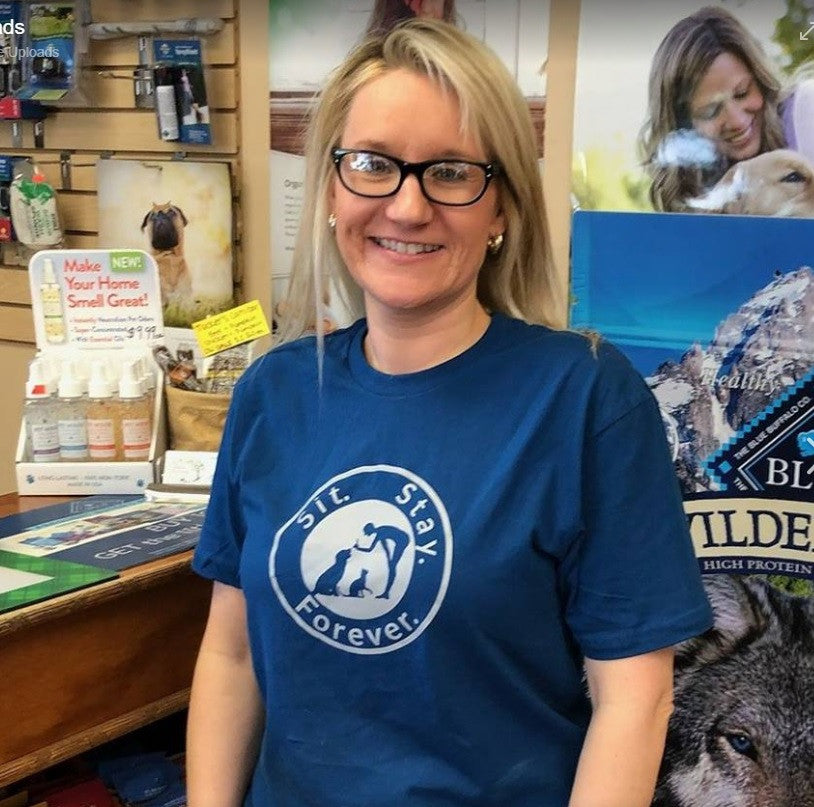 Woman smiling and wearing a blue colored 100% Cotton T shirt with Sit.Stay.Forever. light blue logo positioned in the center of the shirt