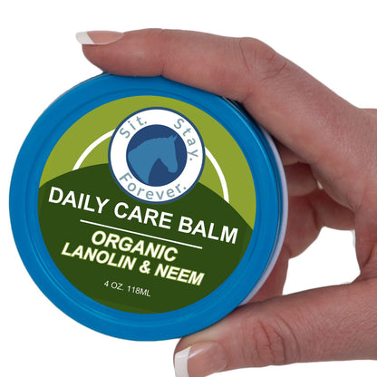 A hand holding a round blue tin of Sit Stay Forever Daily Care Balm Organic Lanolin & Neem against a white background.