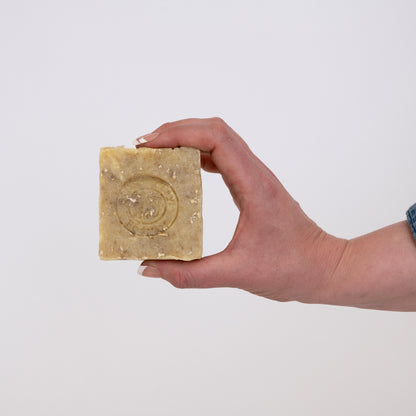 A hand holding a bar of Sit.Stay.Forever pet soap, showing the logo embossed on the soap.